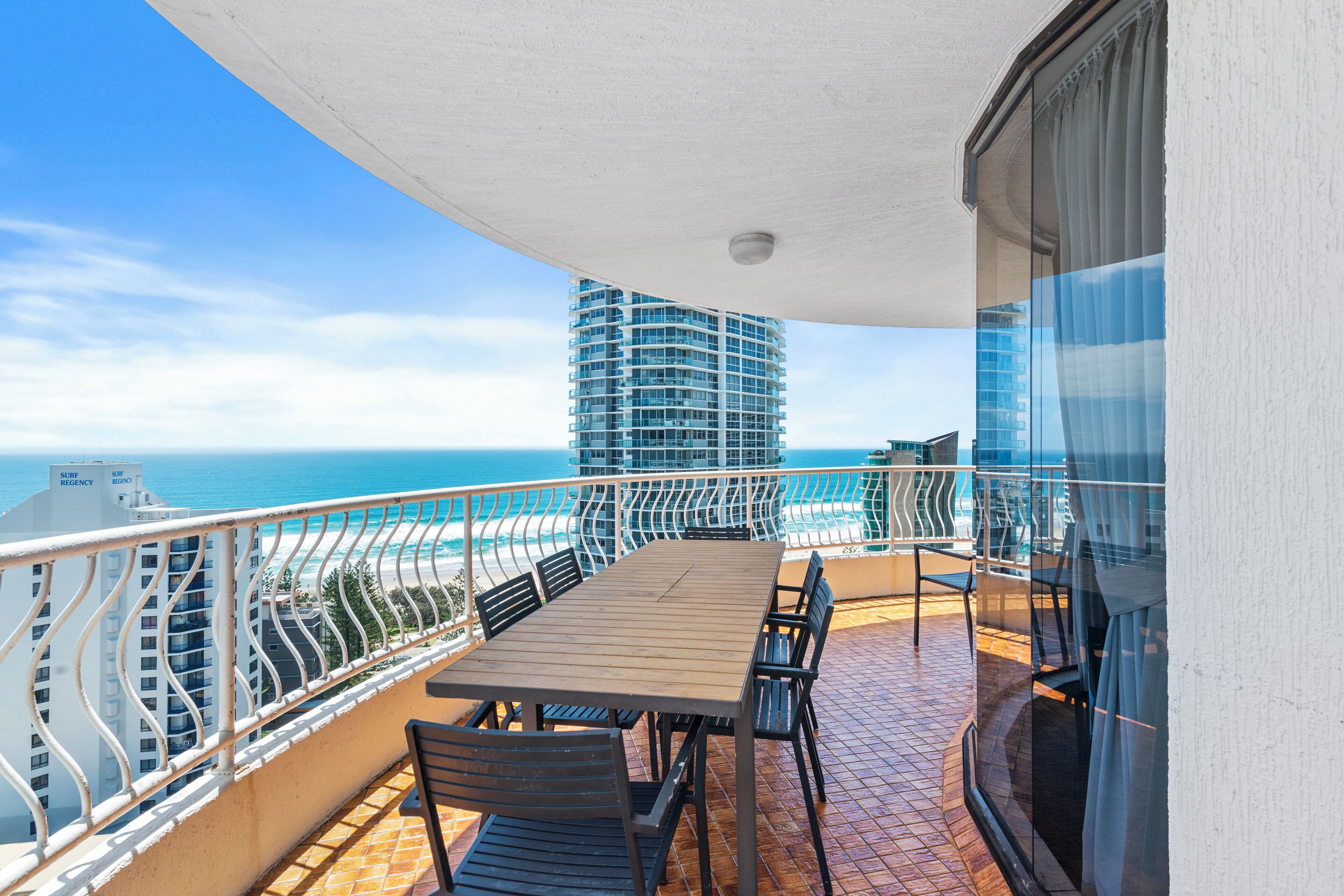 A balcony with a table and chairs, overlooking a beach and ocean.