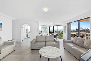 Una sala de estar moderna con un sofá, una mesa de centro y vistas de un paisaje urbano a través de grandes ventanales.