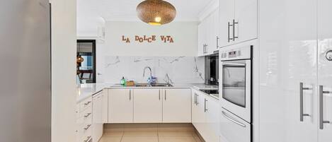 Una cucina moderna con mobili bianchi, uno schienale in marmo e un cartello con su scritto 'LA Dolce Vita'.