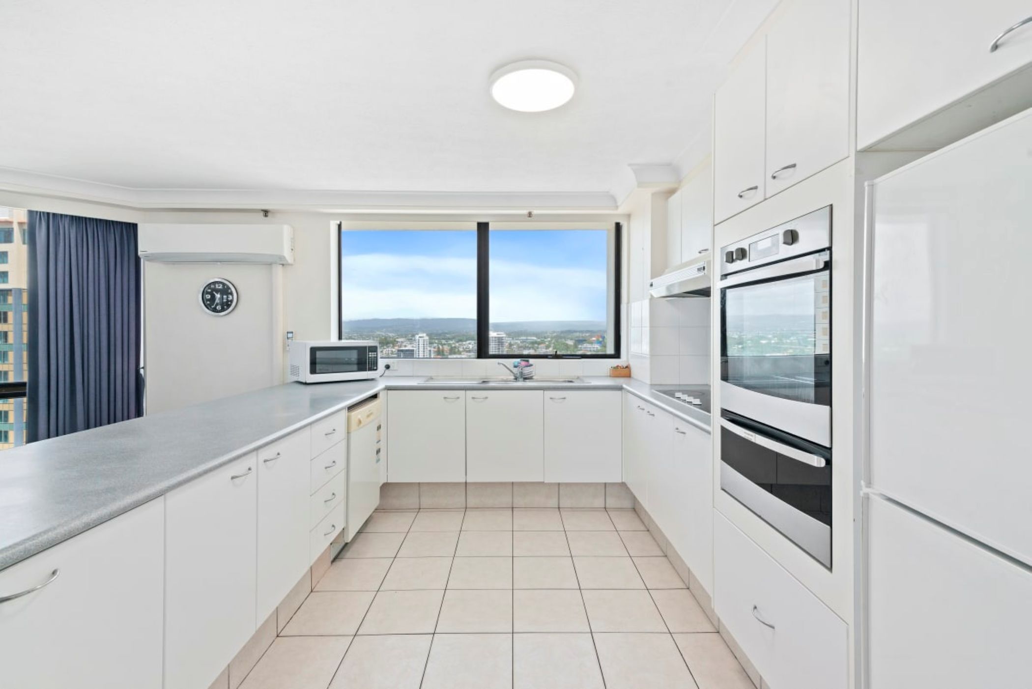 A modern kitchen with white cabinets, a microwave, an oven, and a window with a city view.