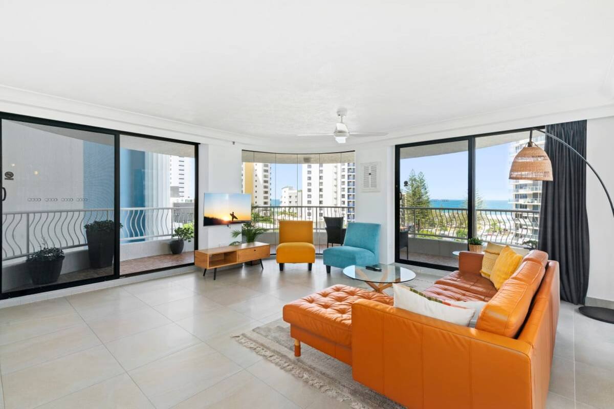 A modern living room with a sofa, armchairs, and a coffee table. There is a balcony with a view of the city.