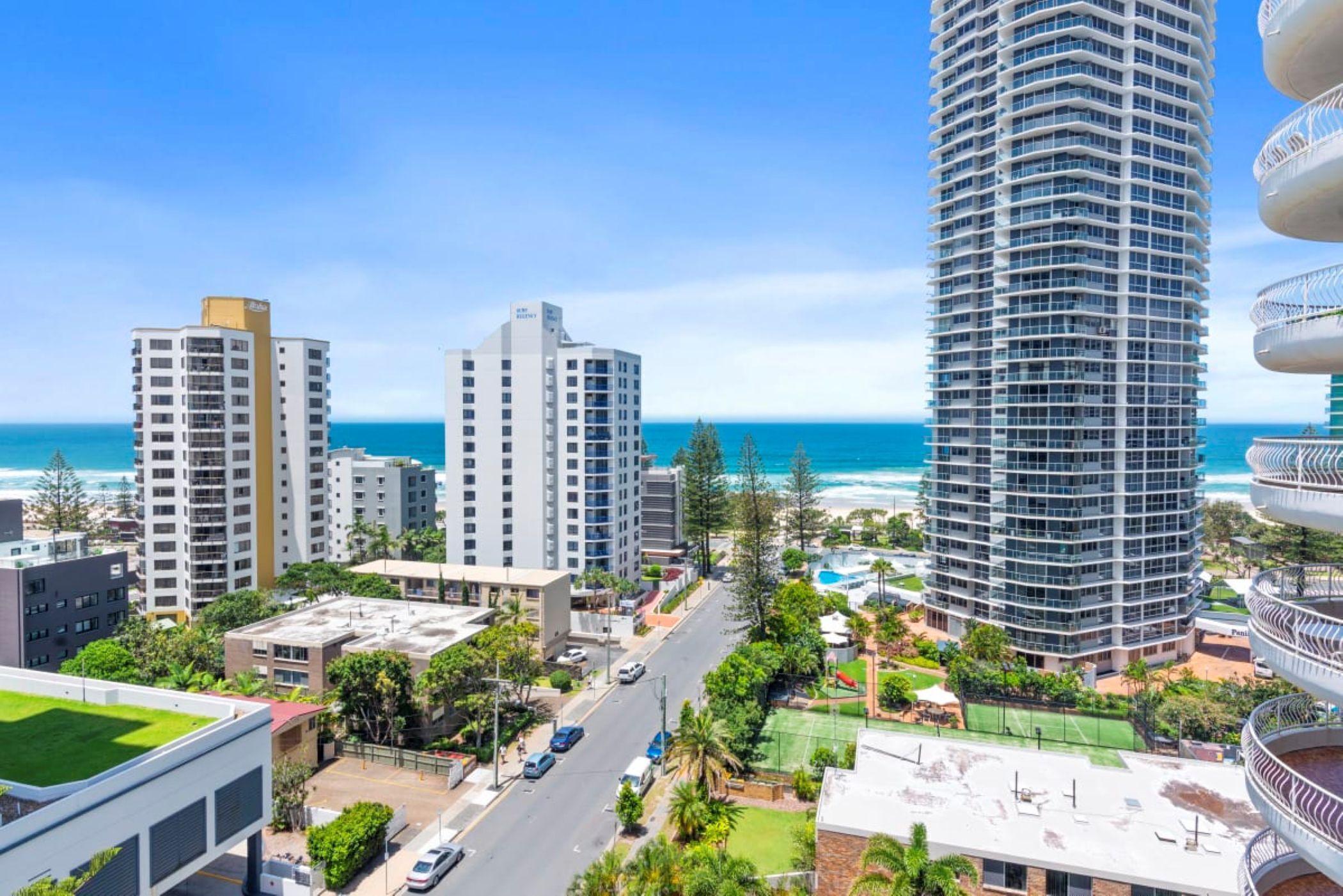 A high-rise hotel with multiple balconies, a view of the ocean, and a well-maintained rooftop garden.