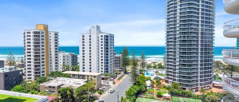A high-rise hotel with multiple balconies, a view of the ocean, and a well-maintained rooftop garden.