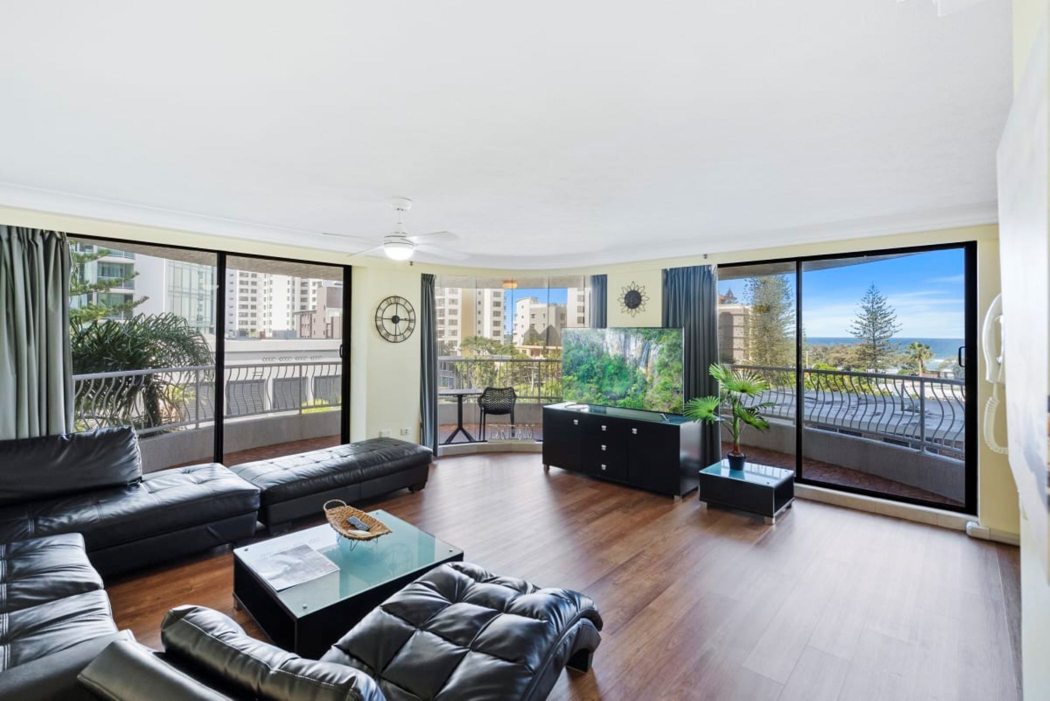 A spacious living room with a large window, a ceiling fan, and a view of the cityscape.