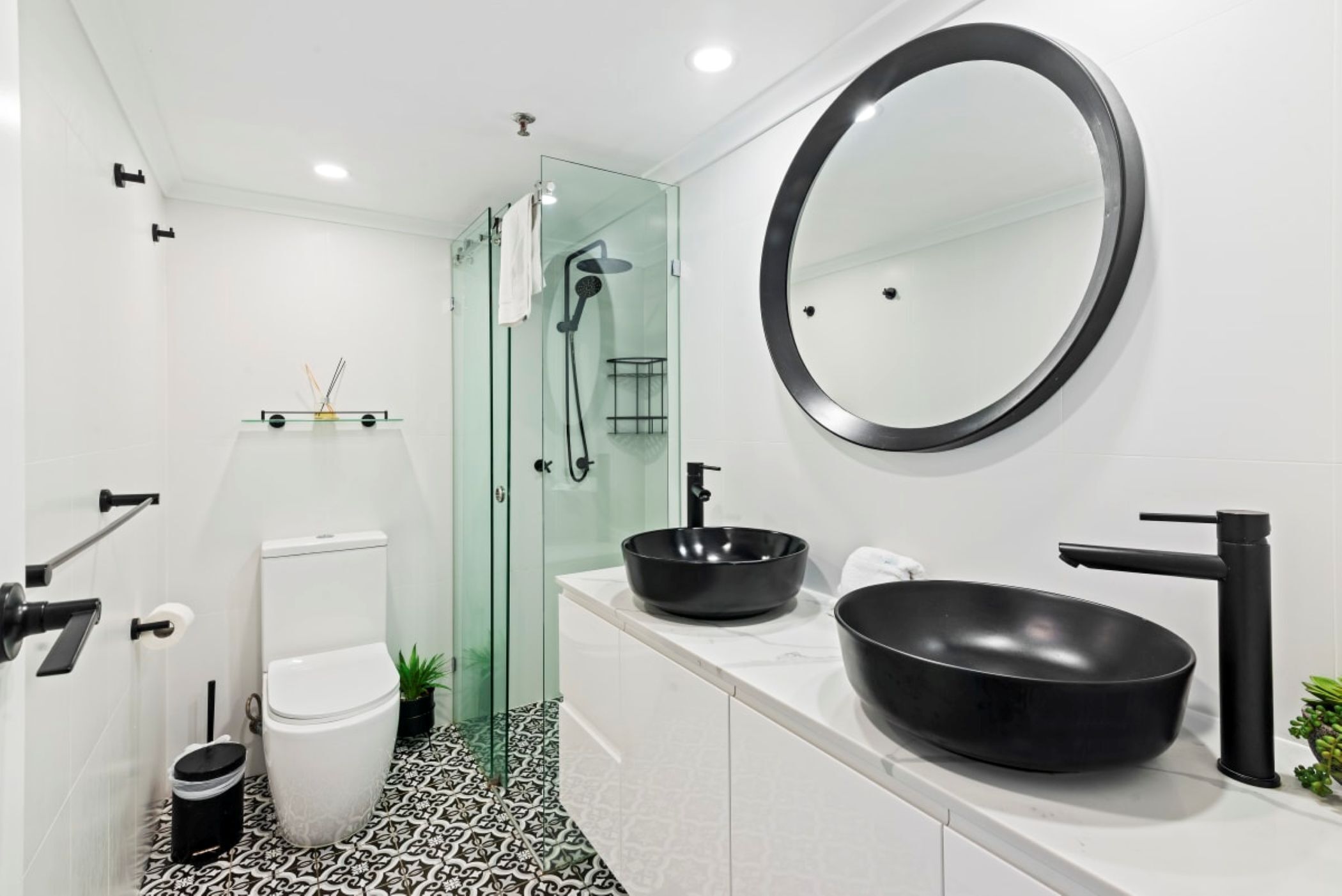 Et moderne badeværelse med toilet, bidet og et stort rundt spejl.