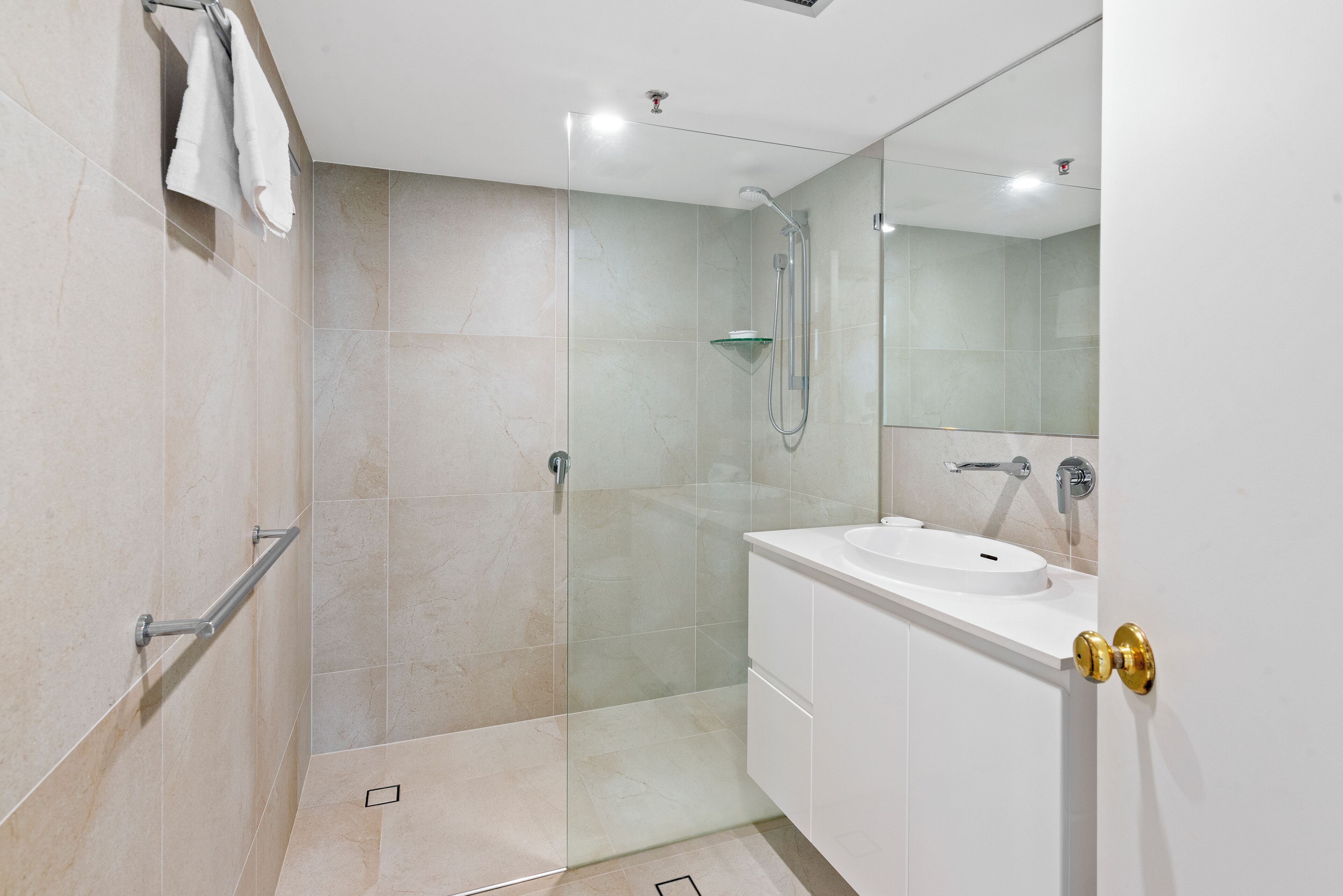 Une salle de bain moderne avec une douche à parois de verre, un lavabo blanc et un meuble-lavabo doté d'une poignée de porte dorée.