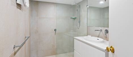 Een moderne badkamer met een douchecabine van glas, een wit wastafelmeubel en een kast met gouden deurklink.