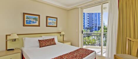 A hotel room with a bed, two paintings on the wall, a nightstand, a chair, and a balcony with a view of buildings.