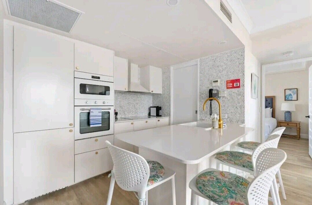A modern kitchen with white cabinetry, a central island, and a seating area with patterned chairs.
