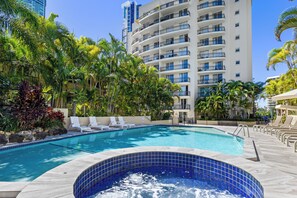 A hotel pool area with a hot tub, lounge chairs, and a tall building in the background. - Palazzo Colonnades (Surfers Paradise)