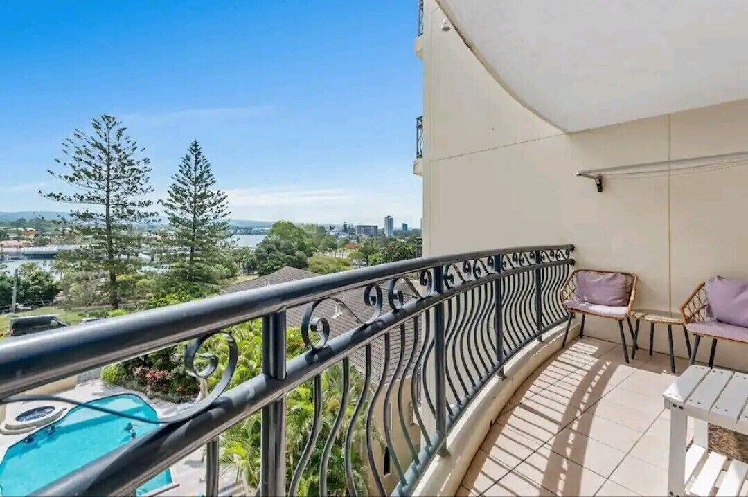 Un balcón con piscina, mobiliario exterior y vistas a árboles y al paisaje urbano.