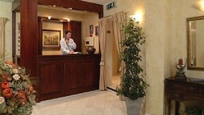 A reception area with a wooden reception desk, a framed picture on the wall, and a potted plant to the right. - Hotel Albert I (Bruges)