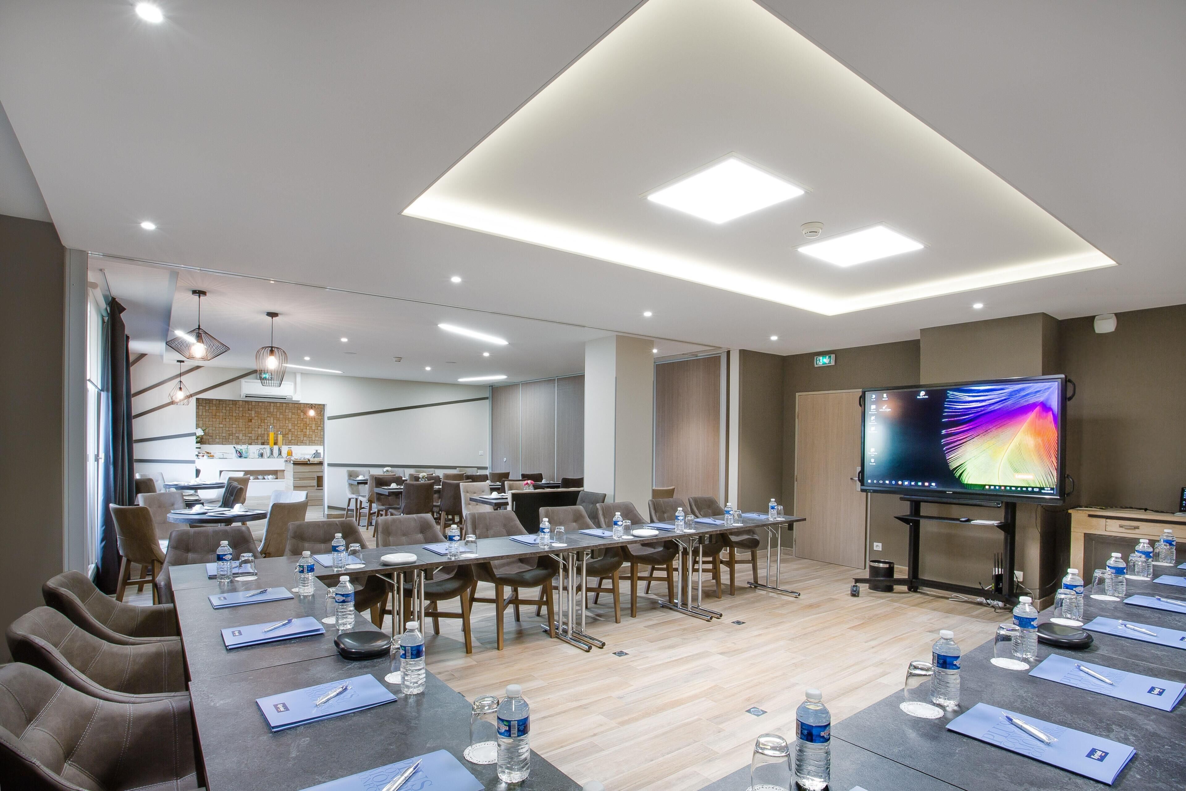 A conference room with a long table, chairs, water bottles, and a flat-screen TV.