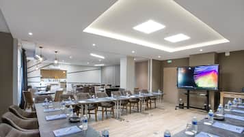 A conference room with a long table, chairs, water bottles, and a flat-screen TV.