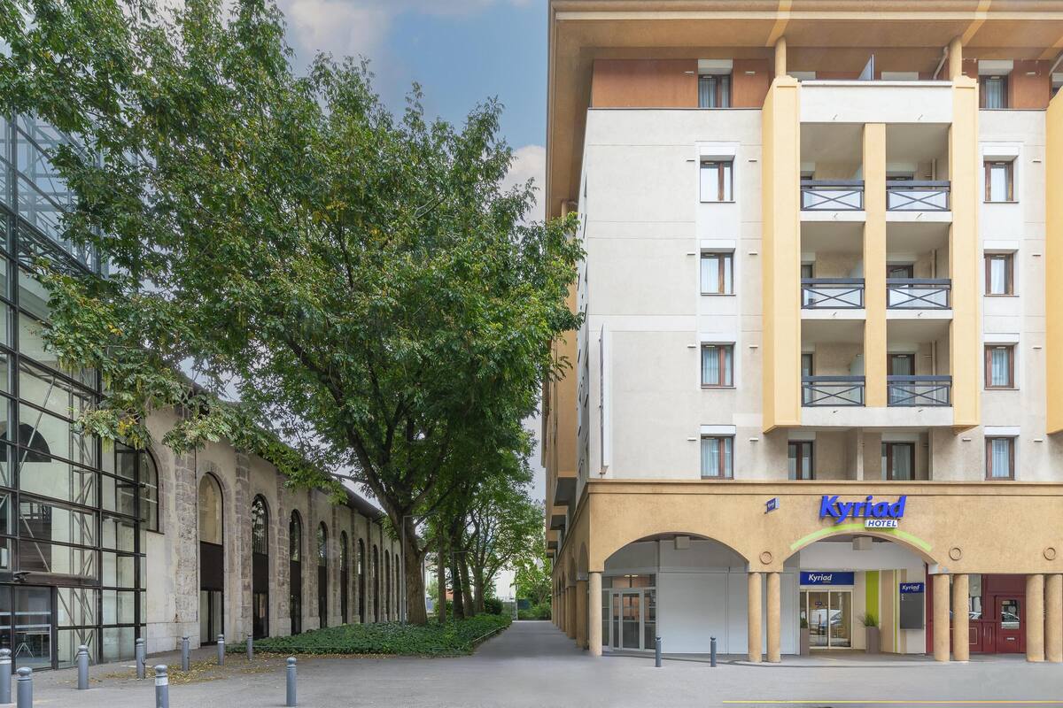 Un hotel con fachada moderna, ventanas en arco y un letrero que dice 'Kyriad Hotel'.