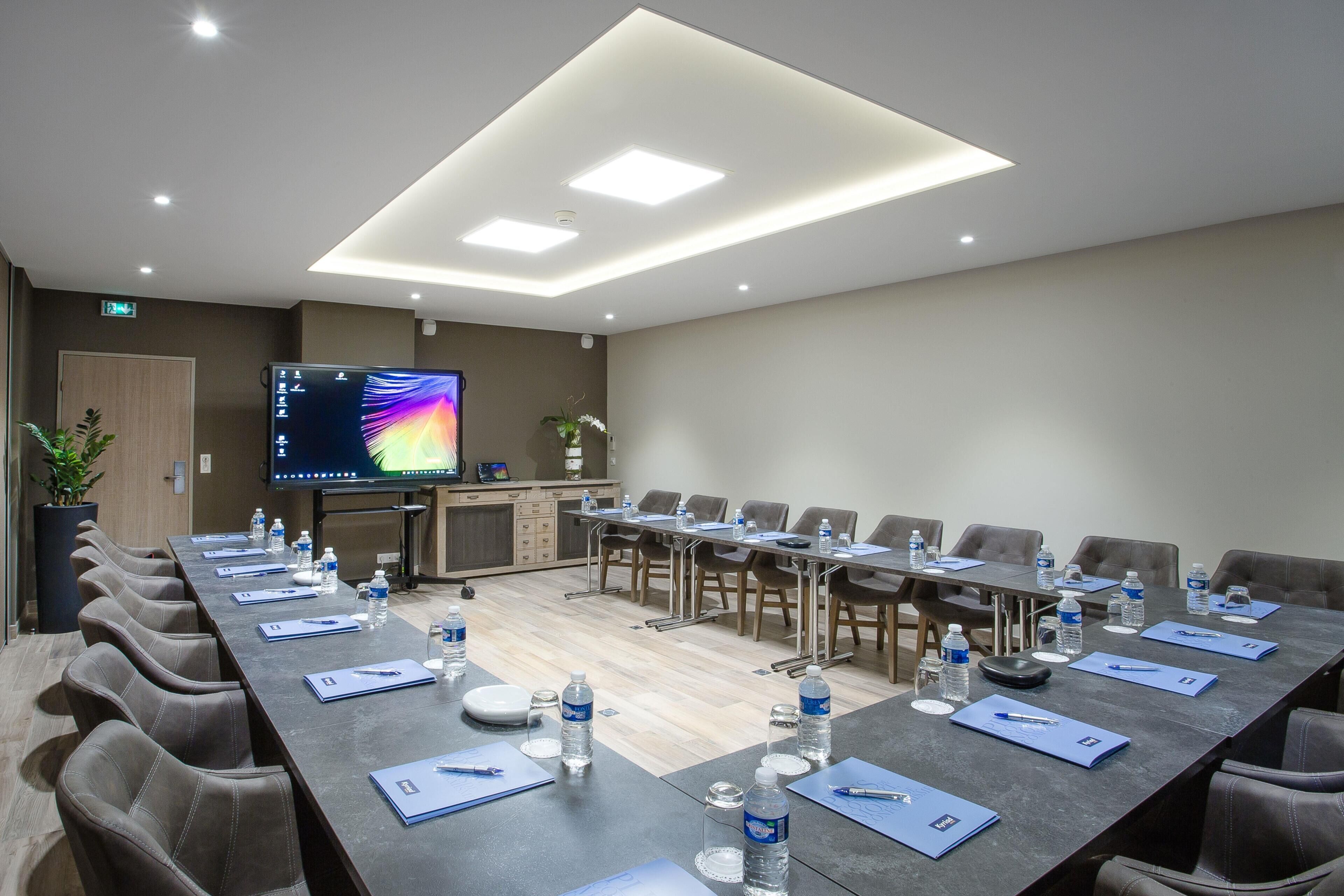 A conference room with a long table, chairs, water bottles, and a screen.