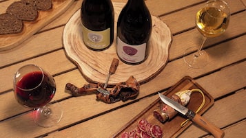 Ein Holztisch mit zwei Weinflaschen, einem Glas Rotwein, einem Glas Weißwein und einem Schneidebrett mit geschnittenem Fleisch und einem Messer.