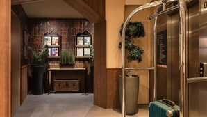 A hotel lobby with a reception desk, a large potted plant, a suitcase, and an elevator. - Kyriad Chambéry Centre - Curial (Chambery)