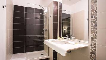 Un baño moderno con ducha envuelta en vidrio, un lavabo blanco y un espejo.
