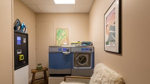 A laundry room with a washing machine, dryer, and a small table with a green container. - Kyriad Chambéry Centre - Curial (Chambery)
