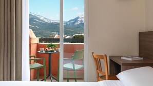 A hotel room with a bed, a wooden chair, a small table with a book, and a balcony with chairs and a table. - Kyriad Chambéry Centre - Curial (Chambery)