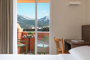 A hotel room with a bed, a wooden chair, a small table with a book, and a balcony with chairs and a table. - Kyriad Chambéry Centre - Curial (Chambery)