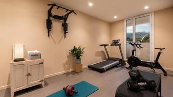 Een huisgymnasium met een loopband, een hometrainer, gewichtsschijven en een optrekstang.