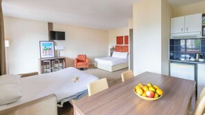 A hotel room with two beds, a dining table with fruit, a TV, and a kitchenette. - Kyriad Chambéry Centre - Curial (Chambery)