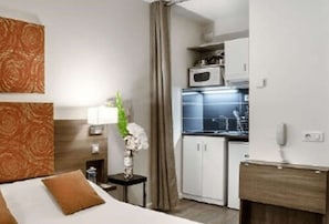 A hotel room with a bed, a small table with a vase of flowers, a microwave, and a kitchenette. - Kyriad Chambéry Centre - Curial (Chambery)