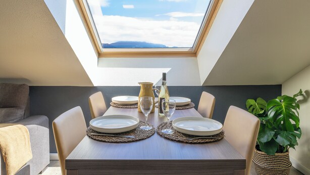 A dining area with a table set for four, a view of the sky through a skylight, and a potted plant on the right. - Kyriad Chambéry Centre - Curial (Chambery)