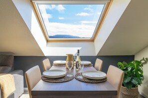 A dining area with a table set for four, a view of the sky through a skylight, and a potted plant on the right. - Kyriad Chambéry Centre - Curial (Chambery)
