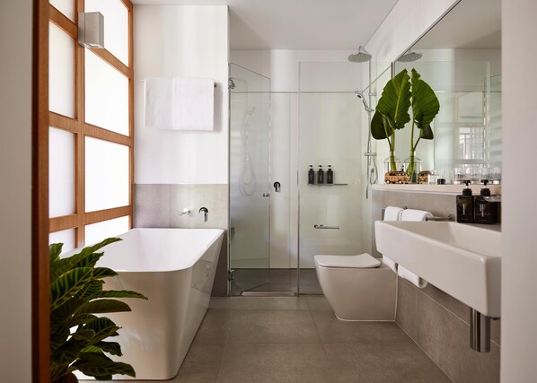 A modern bathroom with a freestanding bathtub, a glass-enclosed shower, a toilet, and a vanity with a large mirror.