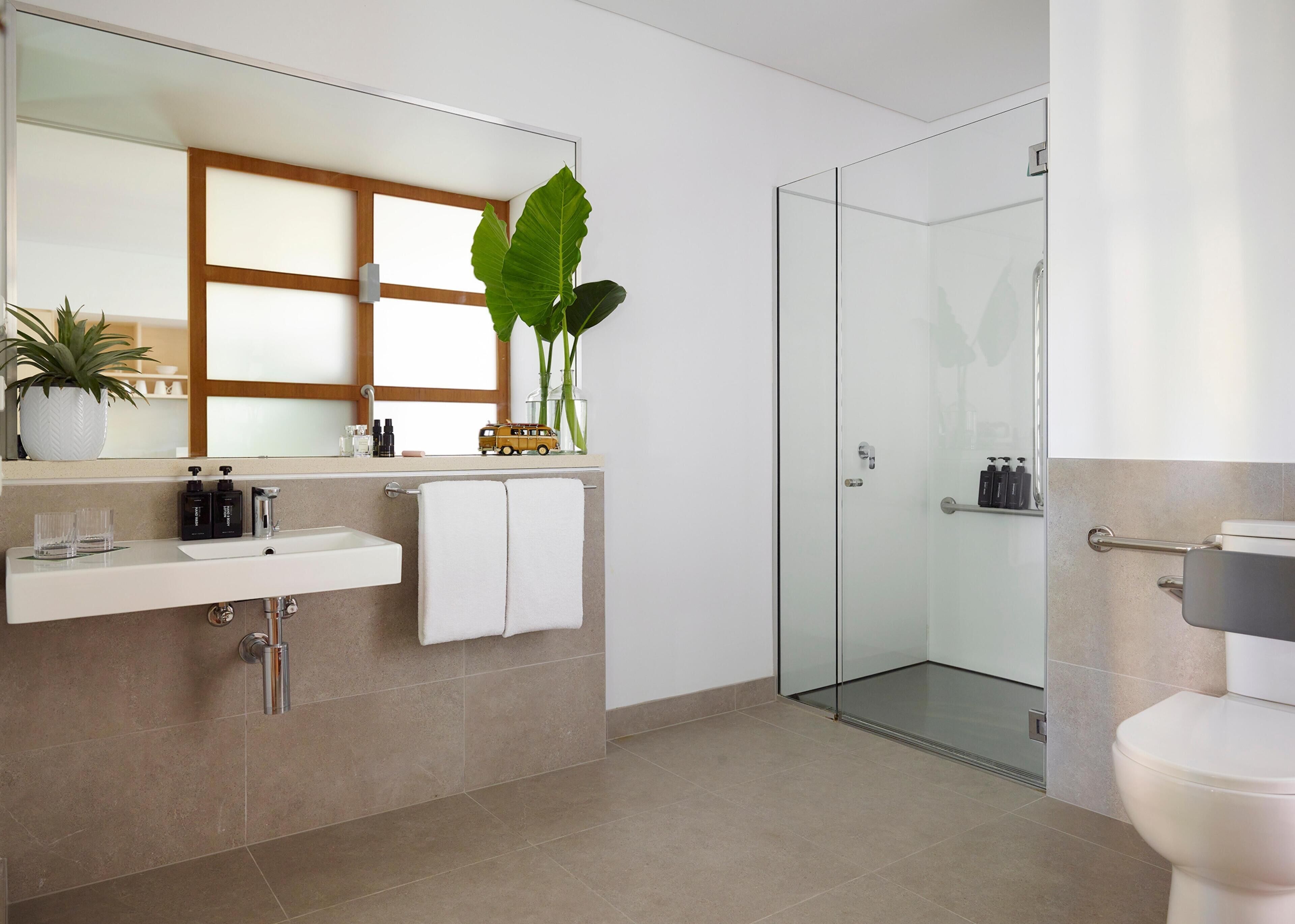 Un baño moderno con cabina de ducha de vidrio, un lavamanos blanco y un espejo grande.