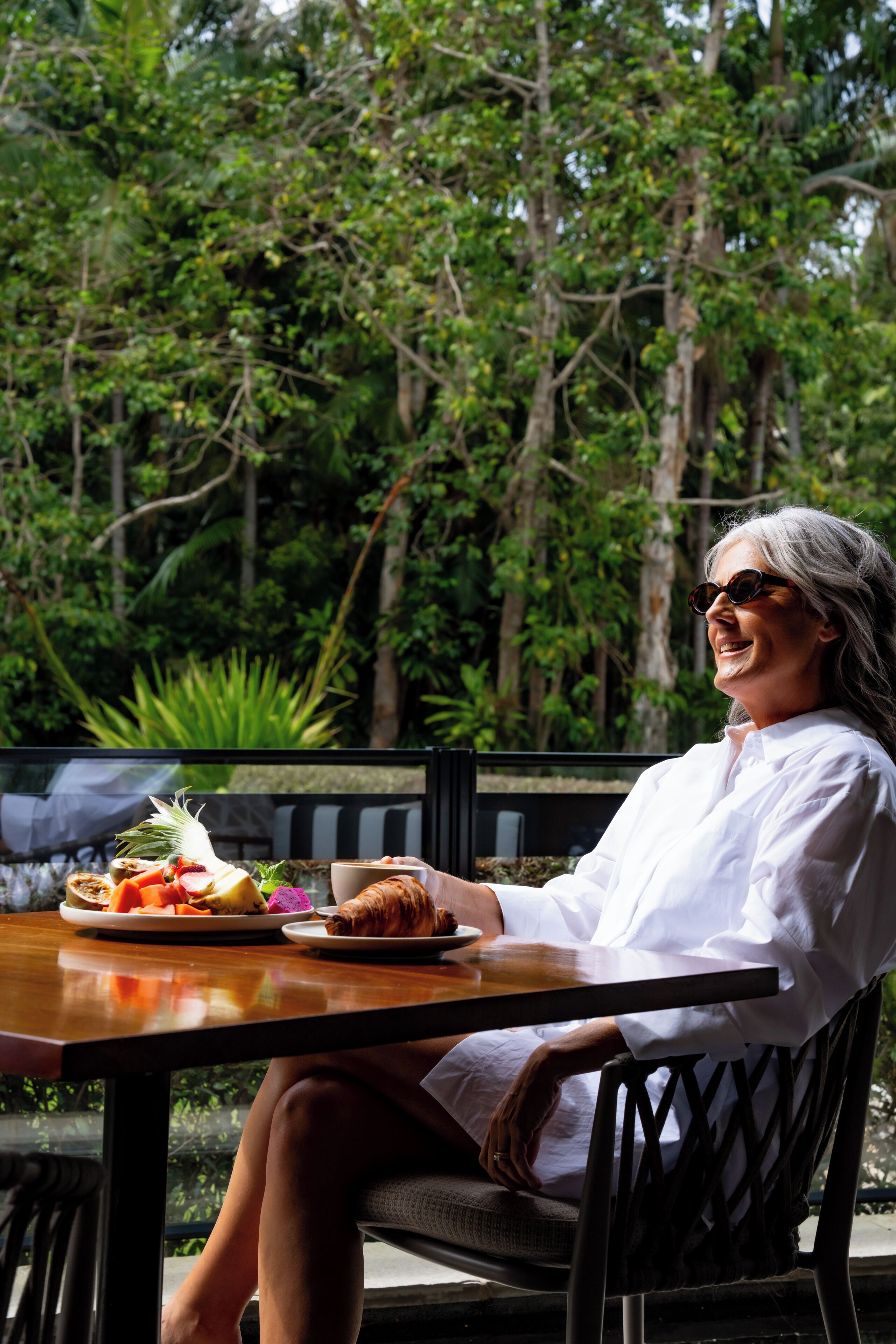 A person seated at a table with a meal, surrounded by greenery.