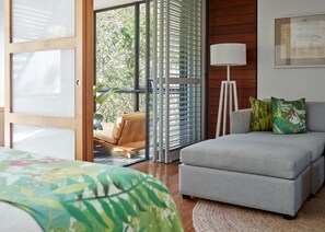 A modern bedroom with a sofa bed, a standing lamp, and a view through a glass door to a balcony.