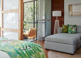 Un dormitorio moderno con sofá cama, una lámpara de pie y vistas al balcón a través de un ventanal.