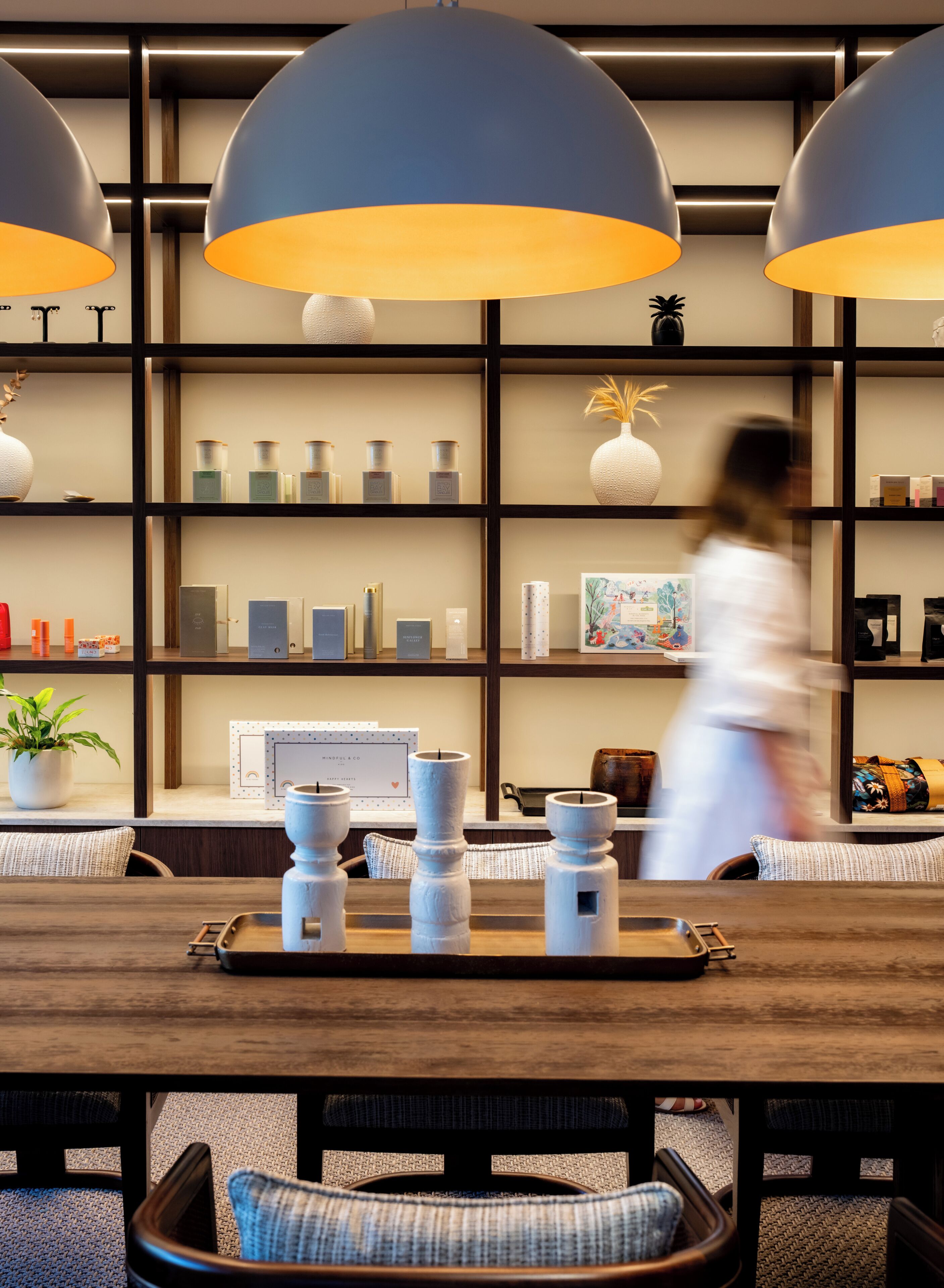 A modern interior with a wooden table, white candle holders, and a shelf with various items.