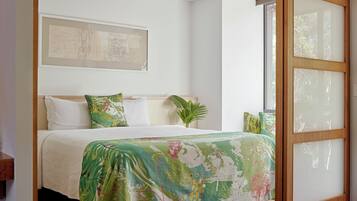 A neatly made bed with a floral bedspread, a large window with a wooden frame, and a wall-mounted artwork.