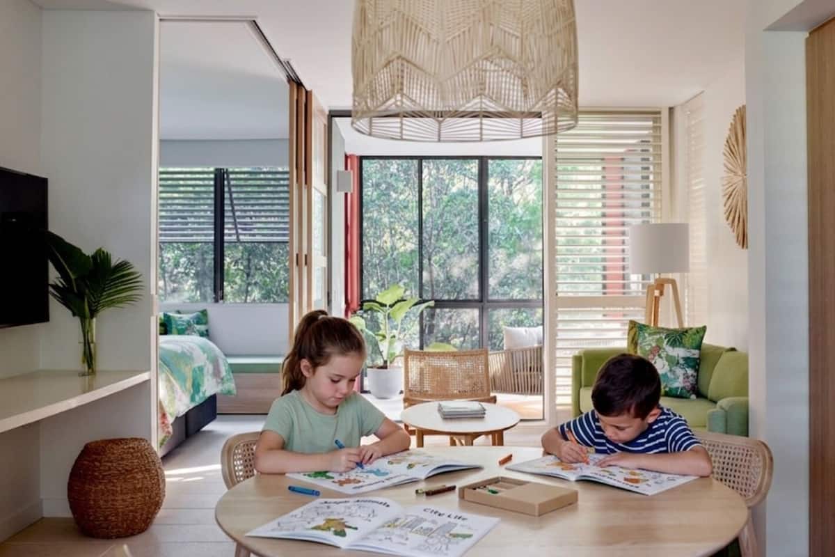 Ein Zimmer mit großem Fenster, einem Esstisch und zwei Kindern, die lernen.