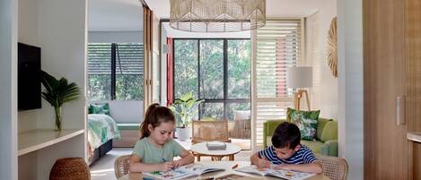 A room with a large window, a dining table, and two children studying.