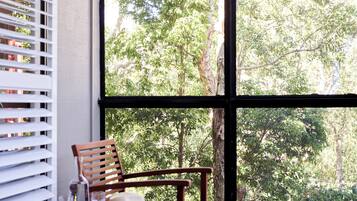 A wooden chair with a hat and glass on a table by a window with blinds.