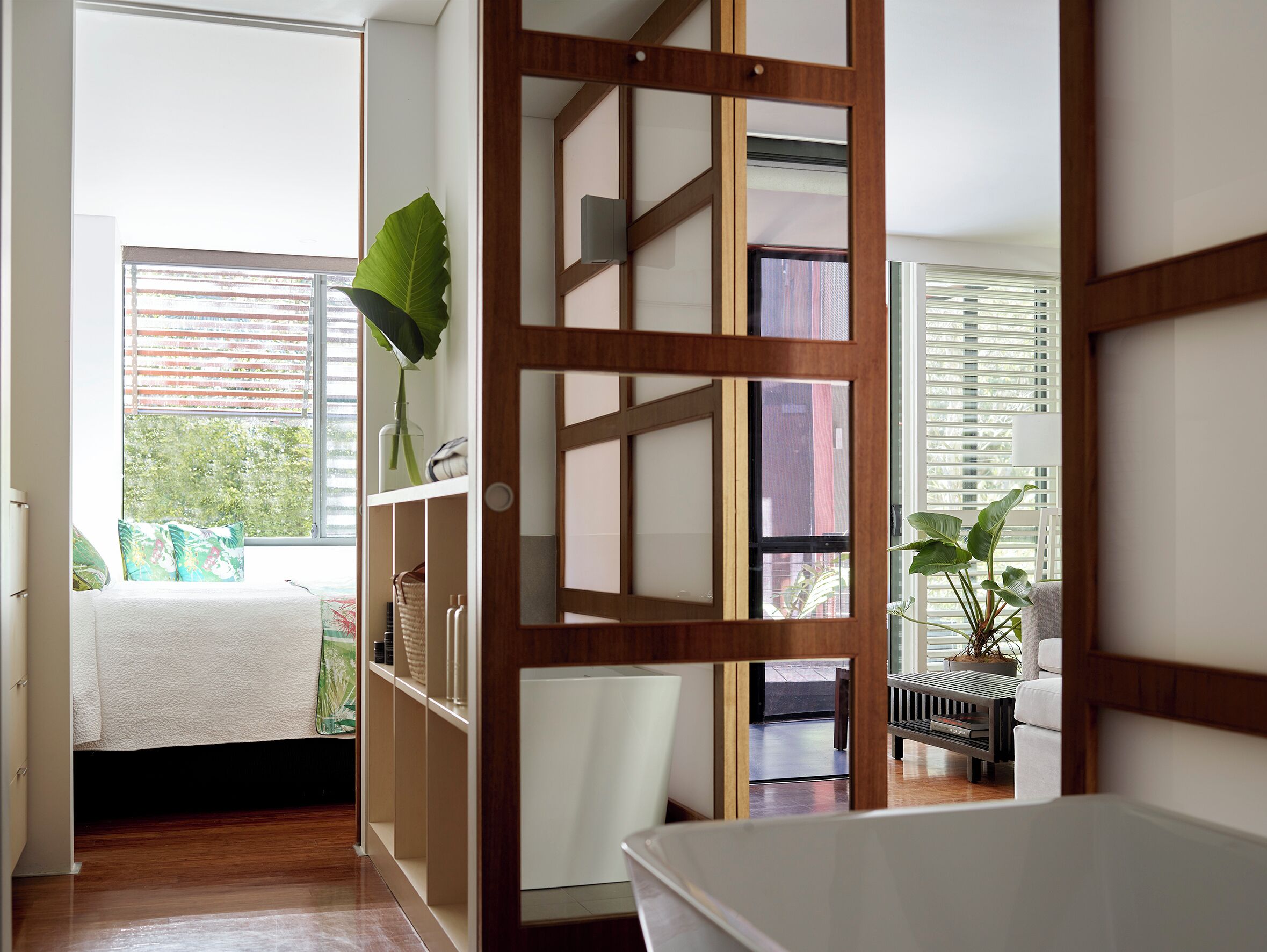A room with a bed, a wooden partition, a window with blinds, and a potted plant.