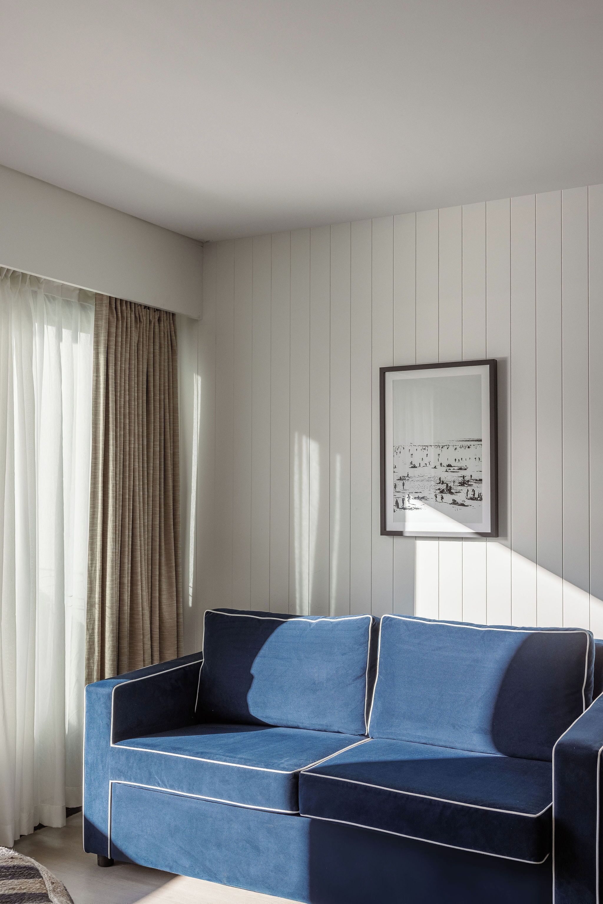 A room with a blue sofa, a framed picture on the wall, and a window with curtains.