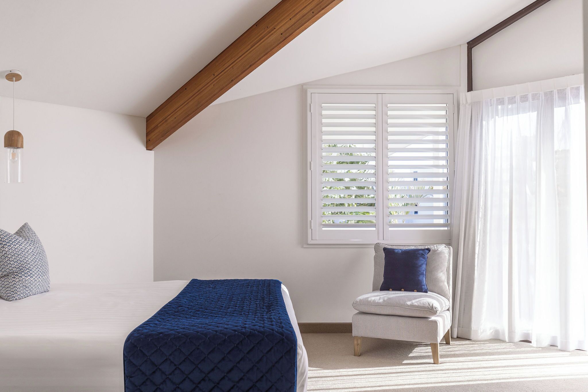 Een slaapkamer met een bed, een stoel, een raam met jaloezieën en een hanglamp.