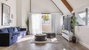 A modern living room with a curved ceiling, a dark blue sofa, two round side tables, and a white cabinet. - Waves Byron Bay (Byron Bay)