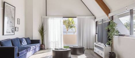 A modern living room with a curved ceiling, a dark blue sofa, two round side tables, and a white cabinet.