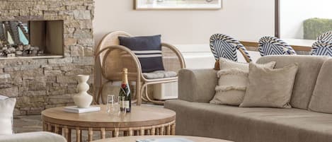 Un salon chaleureux avec un mur en pierre, une table basse en bois, un canapé beige et un fauteuil en osier.