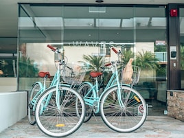 Tres bicicletas turquesa estacionadas frente a un edificio con entrada de vidrio, detector de incendios y un letrero que dice 'No Smoking'.