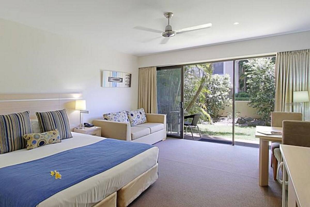 A hotel room with a bed, a sofa, a desk, and a balcony with a view.