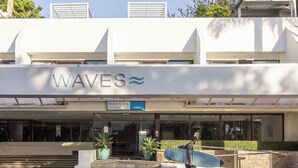 A building with a sign reading "WAVES" and a person carrying a surfboard. - Waves Byron Bay (Byron Bay)